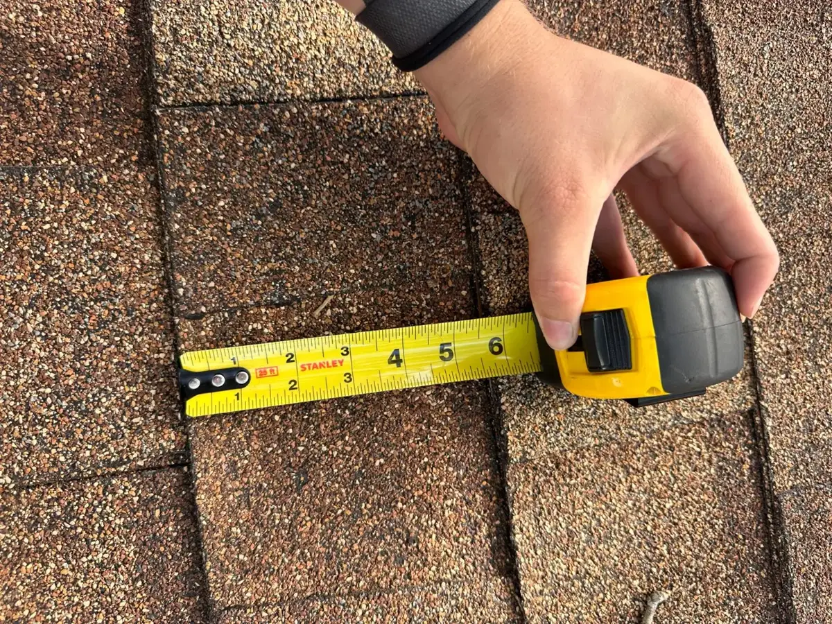 Metro Builders inspector measuring storm damage on a shingle with a tape measure